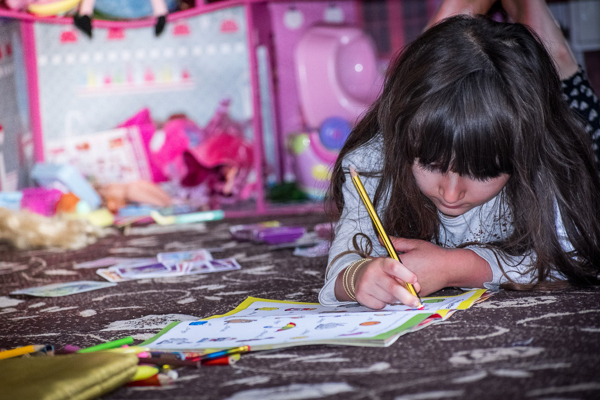 A little girl writes in a workbook among craft supplies