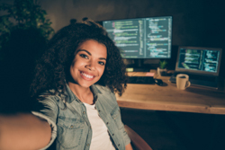 A teenage girl takes a selfie in front of her computer while coding