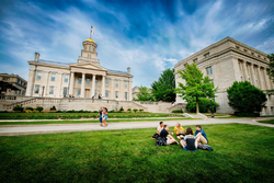A group of people sitting on a lawn in front of a large campus building