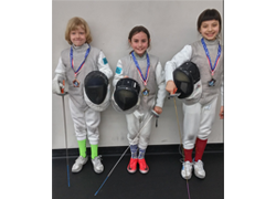 Three students in fencing gear pose wearing their medals after a tournament