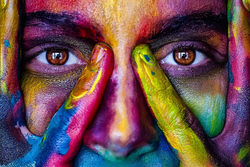 A close-up of a person's face and hands covered in colorful paint
