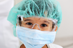 A child wearing goggles, a surgical mask, and a hair net