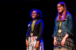Two teenagers standing on a stage wearing medals