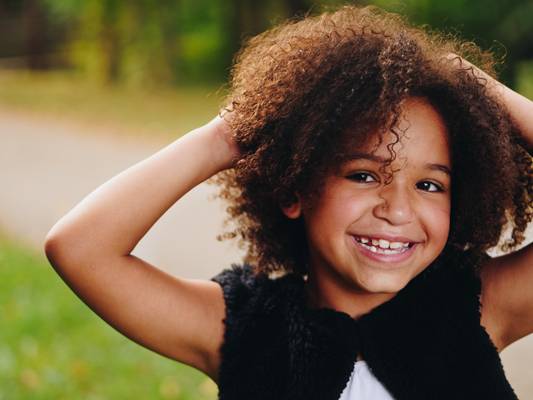 A portrait of a little girl with curly hair smiling