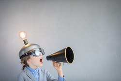 A child wears goggles and a metal cap with an illuminated light bulb on top while shouting into a megaphone