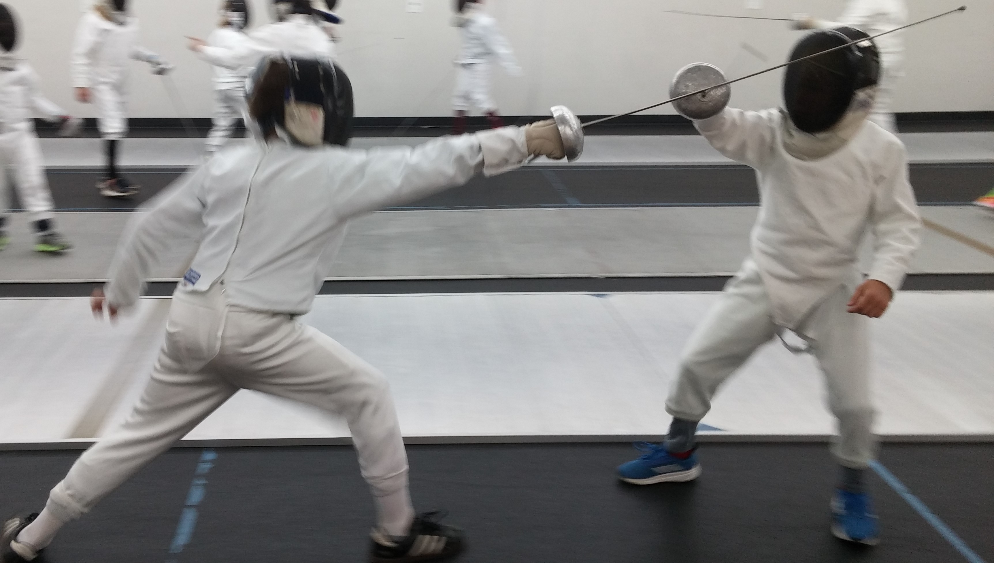 Two children in fencing whites in the middle of a bout