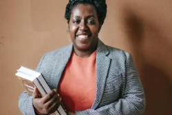 A woman holds books and smiles at the camera